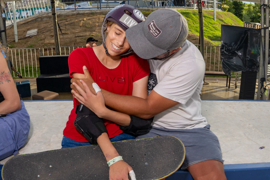 Ana Aguiar sentada com skate, recebendo abraço